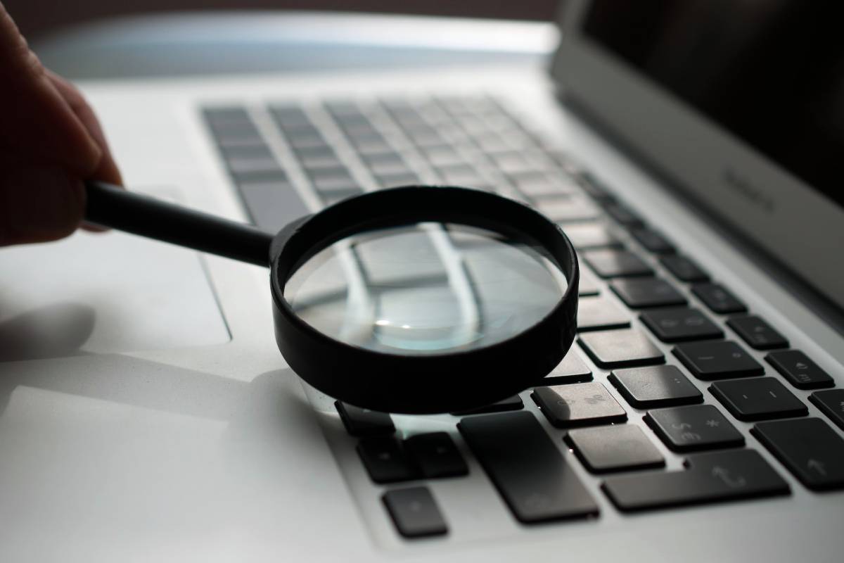 Person inspecting a laptop keyboard with a magnifying glass